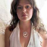 Woman wearing a silver necklace with a circular pendant against a neutral background